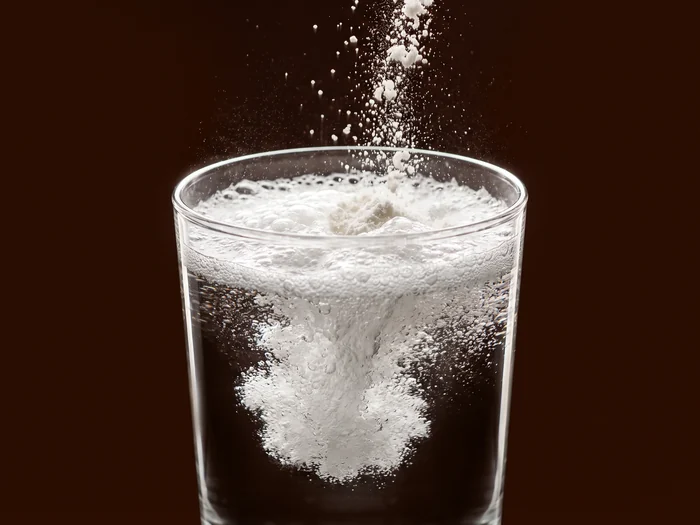 White effervescent foam bursting at the surface of a glass of water, lit against dark brown